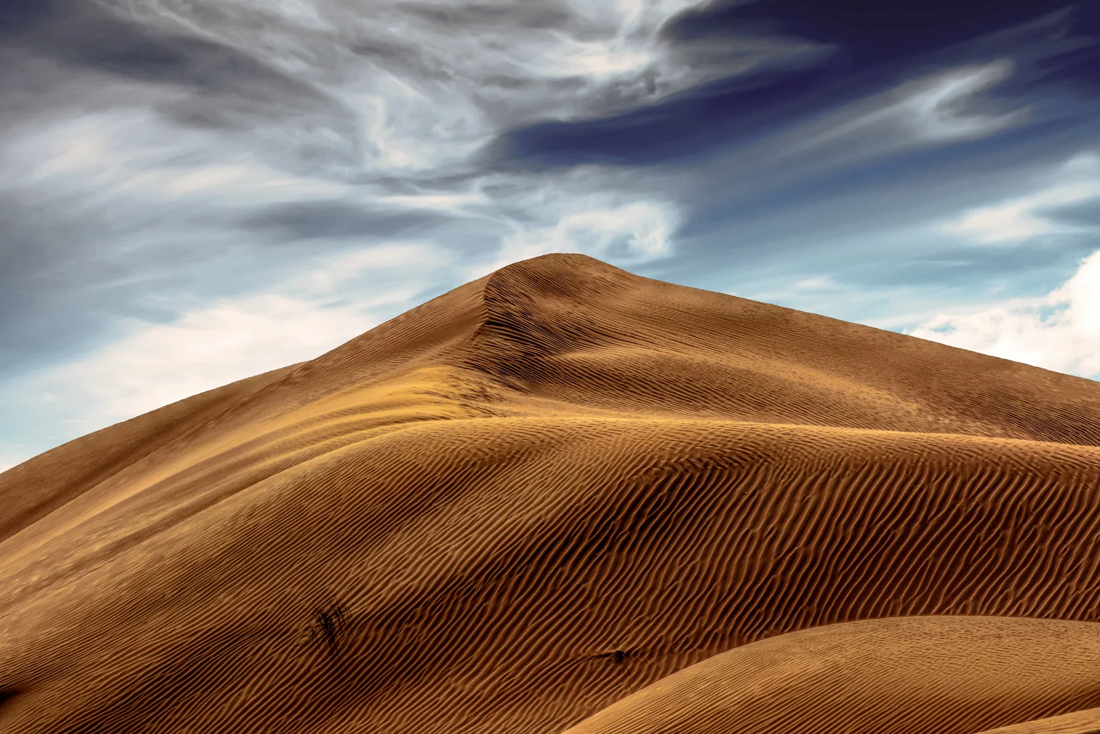Wind-shaped desert dunes beneath a streaked sky