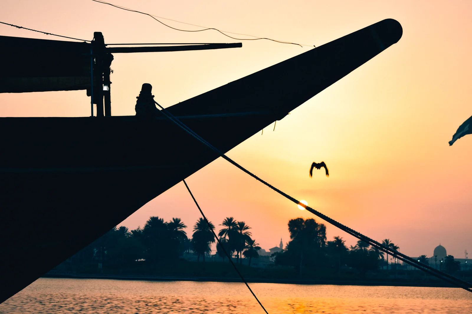 The dark bow of a wooden dhow silhouetted against orange sunset light and water